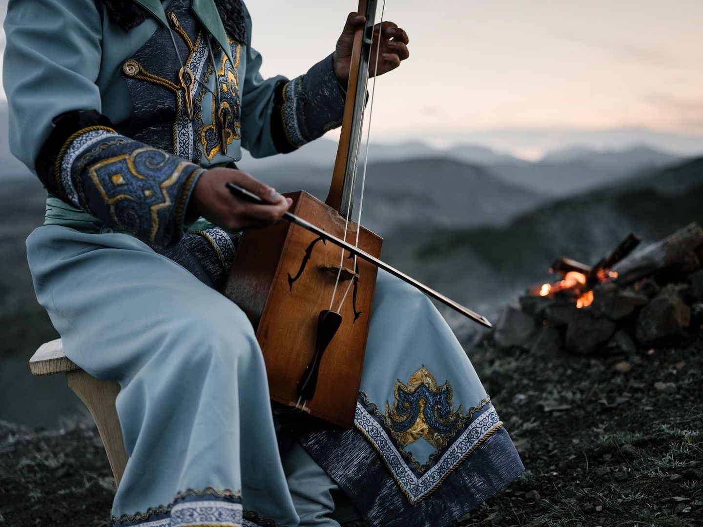Muzikant in traditionele kleding bespeelt een strijkinstrument bij een kampvuur