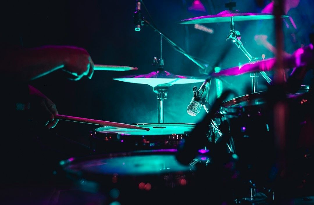 Close-up van een drummer en drumstel onder kleurrijke podiumverlichting